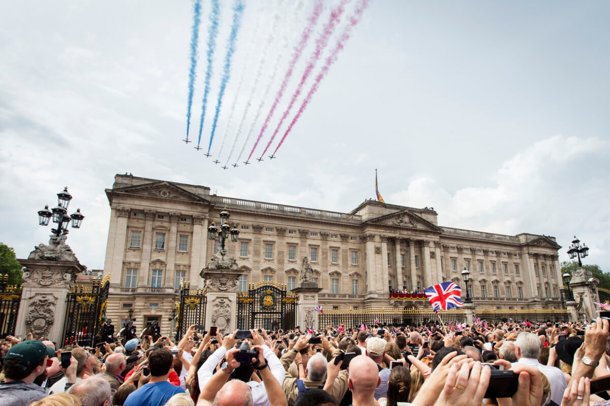 The Red Arrows aerial display team flypast over Buckingham Palace on a royal occasion and crowds in the Mall, London, England.