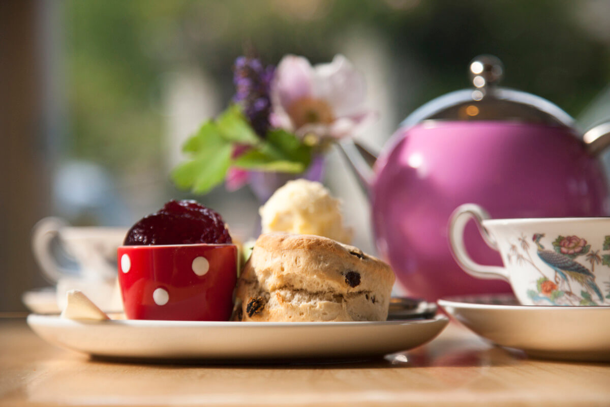 A traditional cream tea laid out on a table inside the Lustleigh Tearooms, with scones, jam and cream. A large pink teapot.