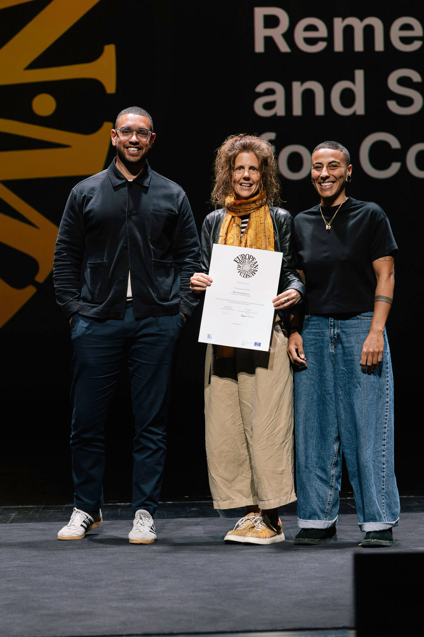 Manchester Museum Director Esme Ward holds certificate on-stage at EMYA2025 with colleagues