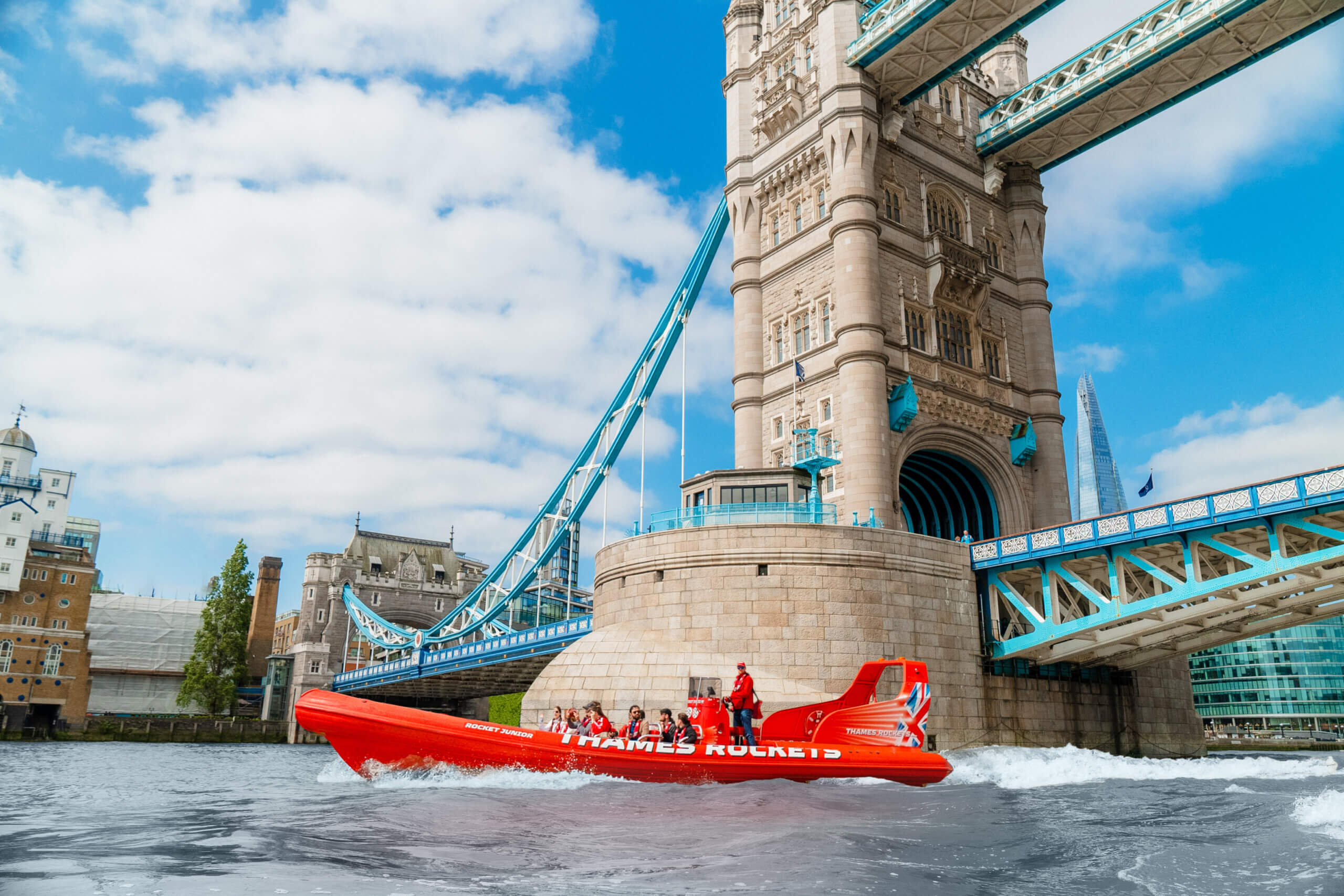 A speedboat with tourists zipping past Tower Bridge