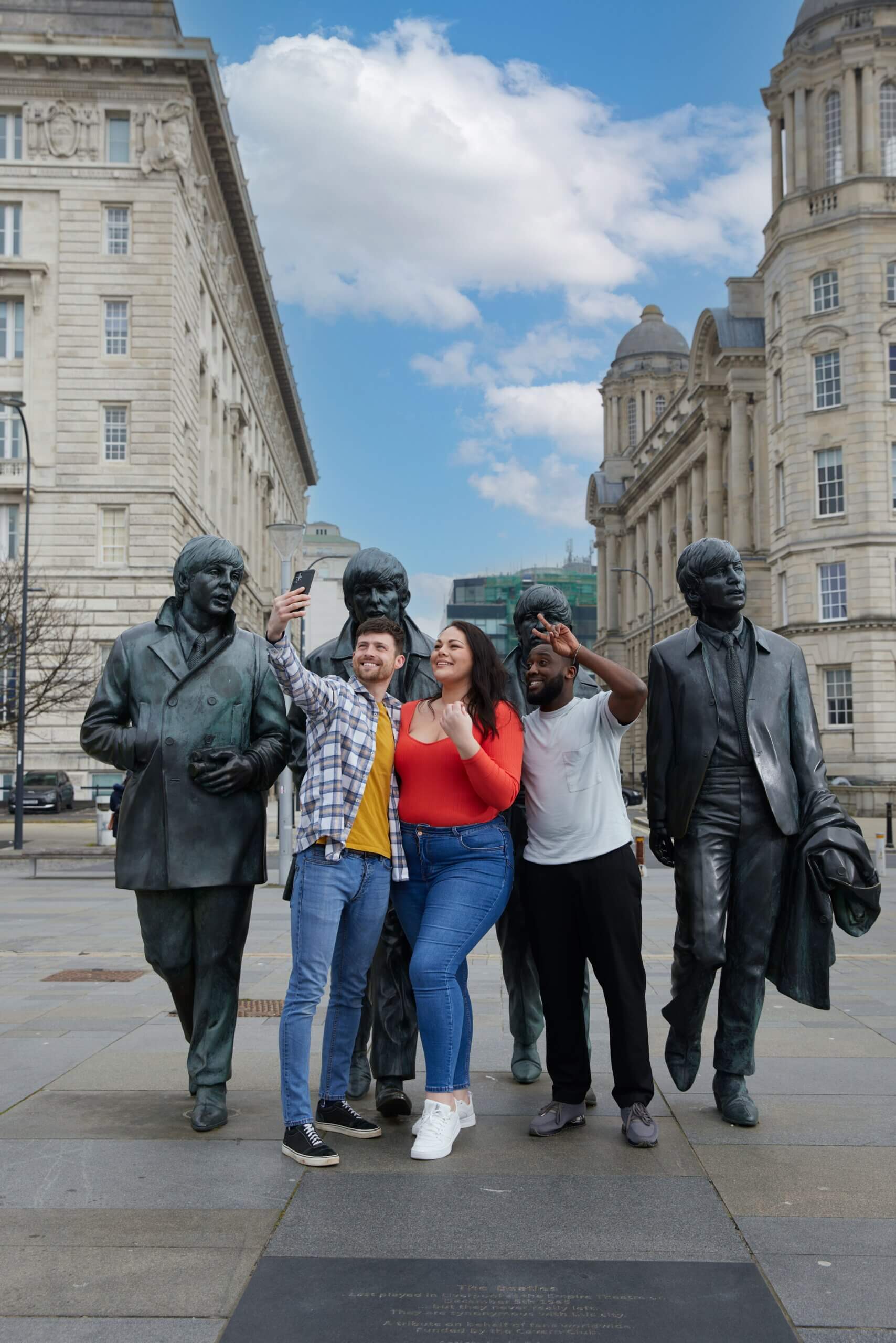 A group of friends, two men and a woman take a selfie in front of a statue of The Beatles, Liverpool Waterfront, Liverpool.