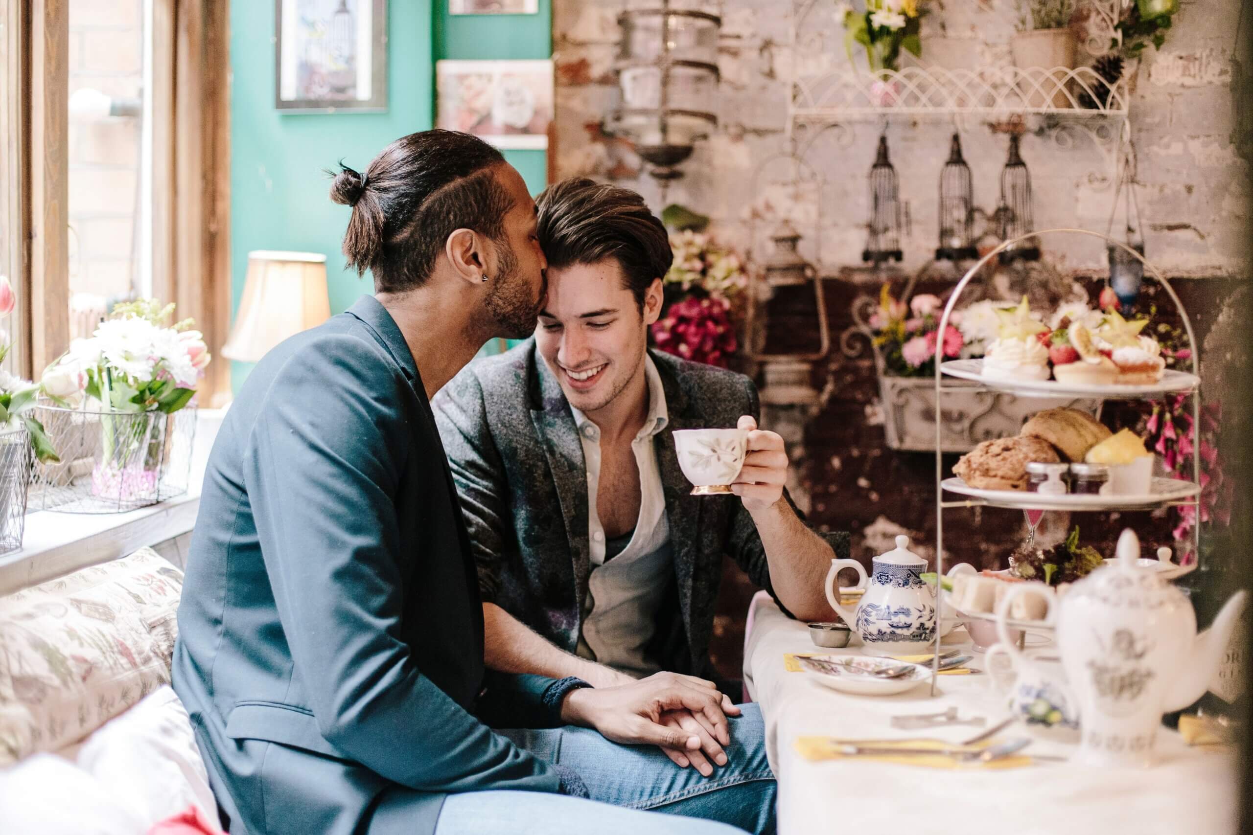 Two men at the Richmond Tea Rooms in Manchester, holding hands and one man is kissing the other man's forehead.