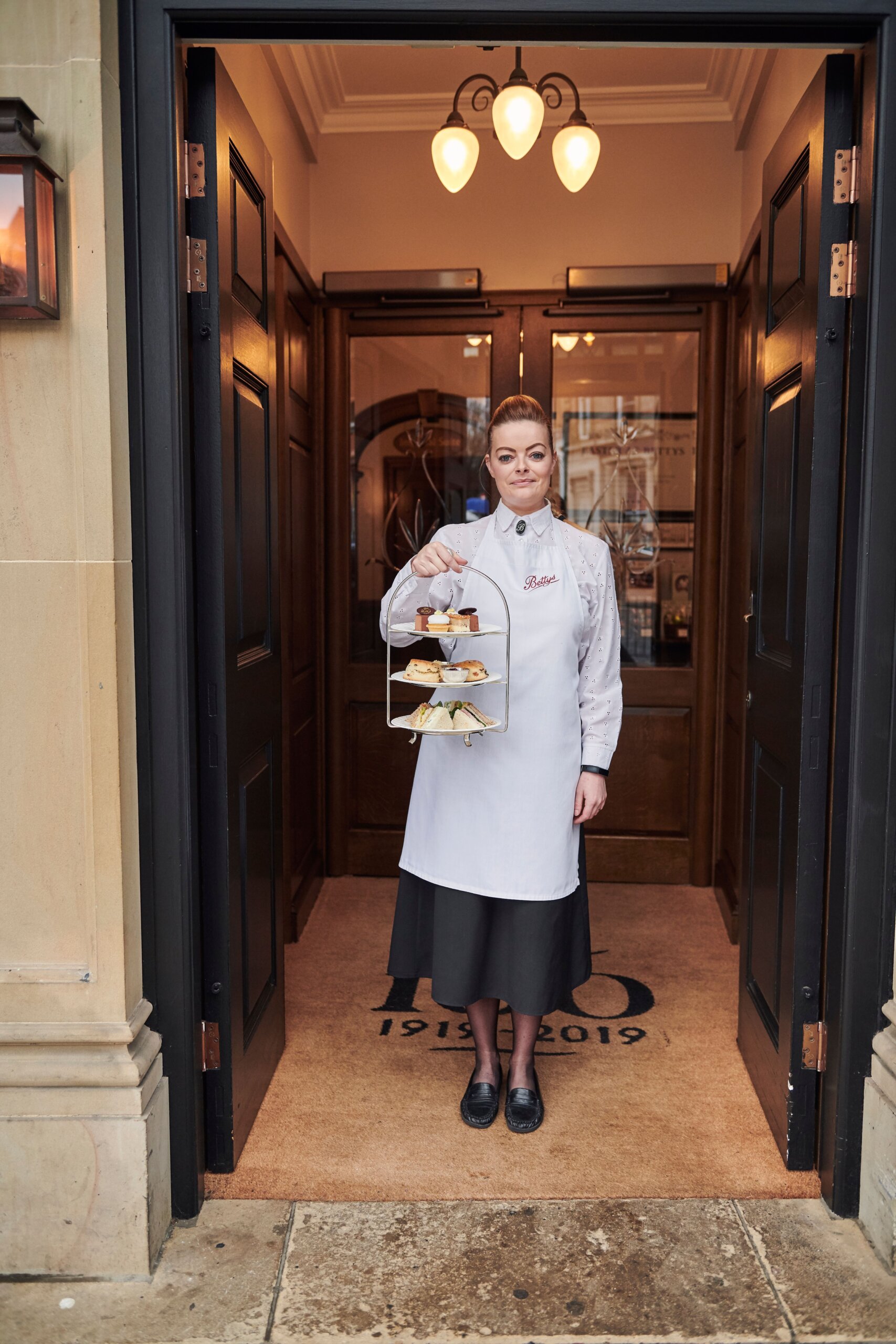 Waitress holding a cake-stand in the doorway of a Betty's Cafe Tea Rooms, Harrogate, North Yorkshire, England.